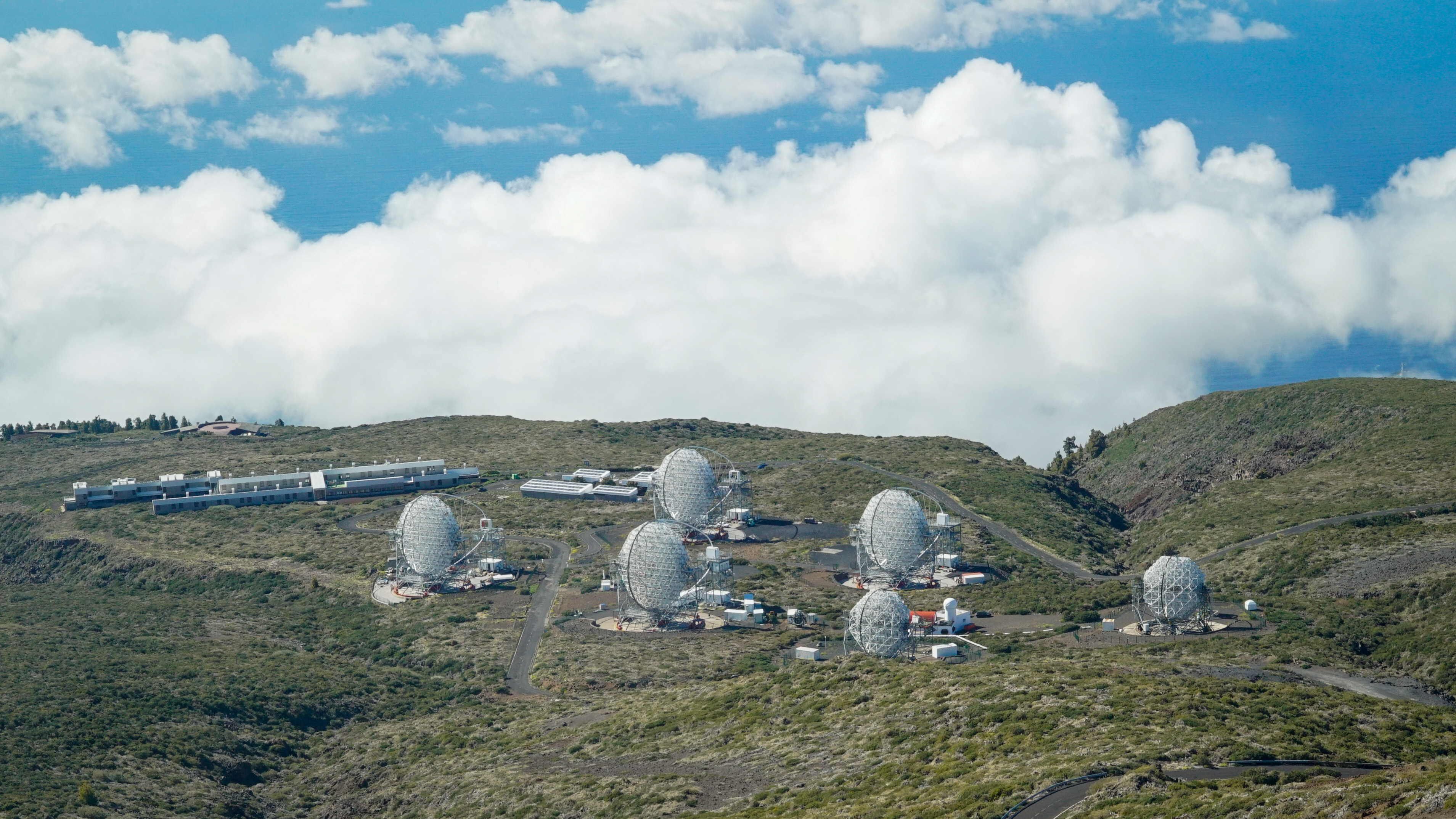 Visión de los 4 LST del CTAO-Norte y los telescopios MAGIC desde lo alto del Roque de los Muchachos. A la izquierda, la Residencia del ORM y, al fondo, el Centro de Visitantes. Crédito: IAC