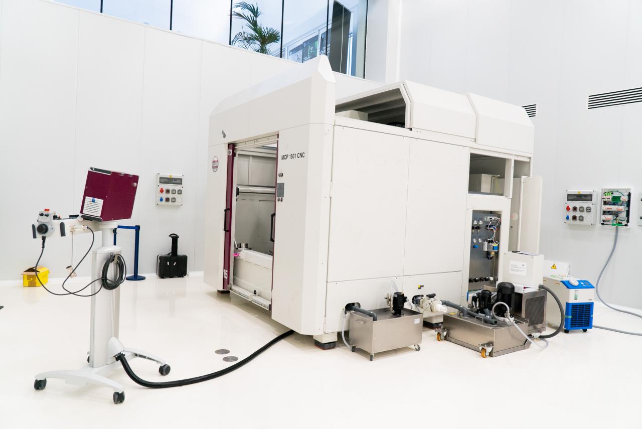 A large white machine with two big doors (polishing machine for large surfaces) in a white room with high ceilings (IACTEC's south clean room).