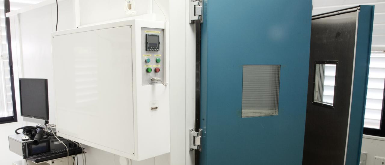 View of the environmental test chamber, a square enclosure with two thick half-open doors and a control panel with buttons, inside the laboratory