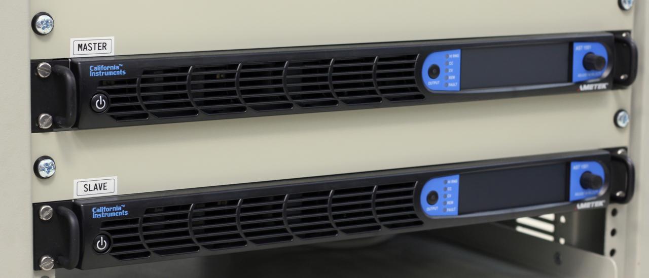 Front detail of the Programmable AC Power Source. Front part of two identical elongated electronic devices with the "master" and "slave" signs, control buttons and ventilation grilles, placed in a rack
