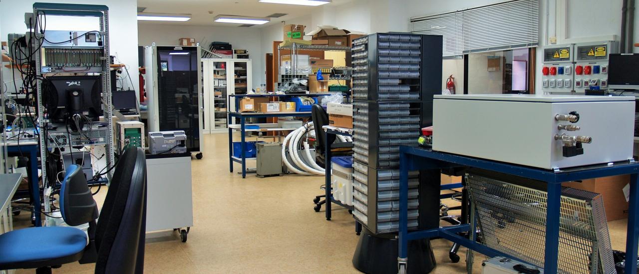 Vista general del laboratorio de diseño electrónico con varios bancos de trabajo, racks de electrónica y armarios para componentes y piezas electrónicas