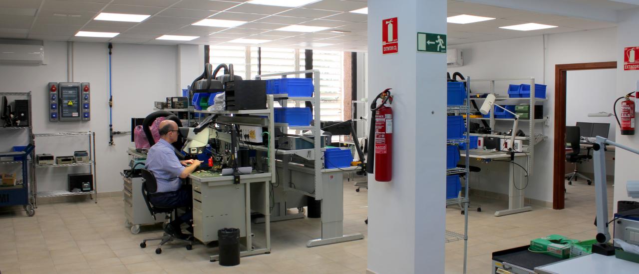 General view of the Electronics Workshop with several workbenches, cabinets and boxes to store components and electronic parts, and a technician working in one of the workbenches