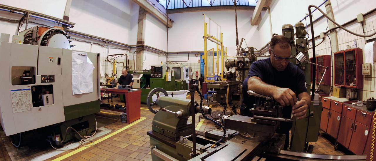 Vista de una parte del taller de mecánica con técnicos trabajando. Autor A. L. Aldai. Amplio taller con varias máquinas de fabricación mecánica y a la derecha un técnico ajustando una pieza en una de ellas