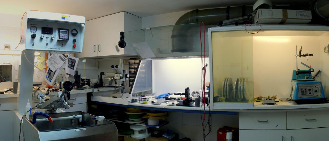 Vista panorámica del laboratorio de fibras ópticas. A la izquierda, máquina para colocar los materiales a pulir con mandos de control en la parte superior y a la derecha, mesas de trabajo con campanas extractoras de gases