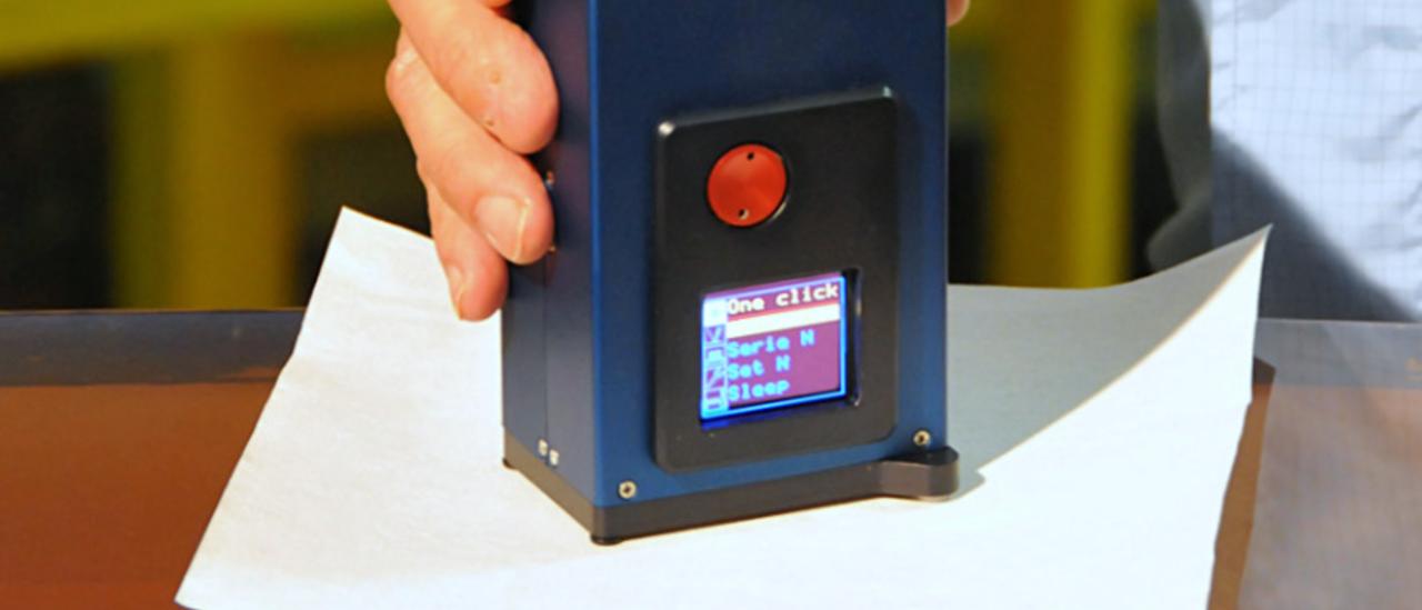 View of the CT7 reflectometer on a mirror. Author A1pixel. Small device with a screen held by a technician's hand on the surface of a mirror