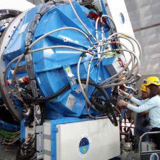 Rear view of the EMIR instrument in GTC with engineers working on the cryogenic system. Large cylindrical structure with metallic tubes and electronic controls