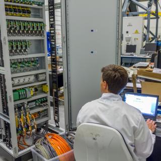 Image of an engineer working on the electronics of the adaptive optics system for GTC in the laboratory Image of an engineer working on the electronics of the adaptive optics system for GTC in the laboratory. Engineer sitting working on a computer with an open electronics cabinet at his side