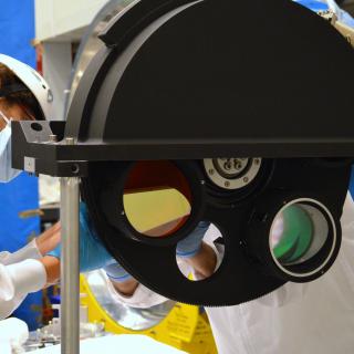Image of an engineer working on the final assembly of the grisms wheel of the EMIR instrument in the laboratory Image of an engineer working on the final assembly of the grisms wheel of the EMIR instrument in the laboratory. Large black metal wheel with holes for optical components