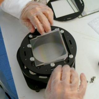 View of an engineer assembling a grism in the laboratory. Engineer placing a piece of glass in a metal cylinder