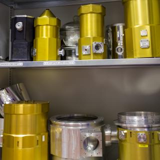 General view of several test cryostats in a laboratory cabinet. Shelves of a cabinet with different metal cylinders fitted with windows and connectors