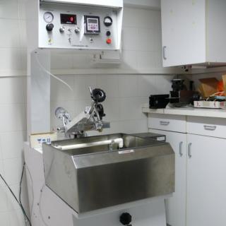 Image of one of the polishing machines in the laboratory. Square machine with a mid-height sine to place the materials to be polished and with metal clamps on top to hold the polishing piece. The control knobs for the machine are in the upper part.